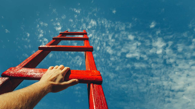 Мужская рука держит красную лестницу на фоне синего неба – Скорпионы в январе 2024 года поднимутся по карьерной лестнице