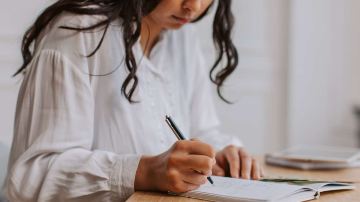 Женщина в белой блузке в тетради ручкой делает анализ своего финансового положения