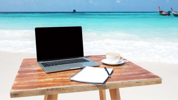 Деревянный стол на берегу моря и на нем ноутбук, тетрадь и чашка кофе – рабочее место фрилансера