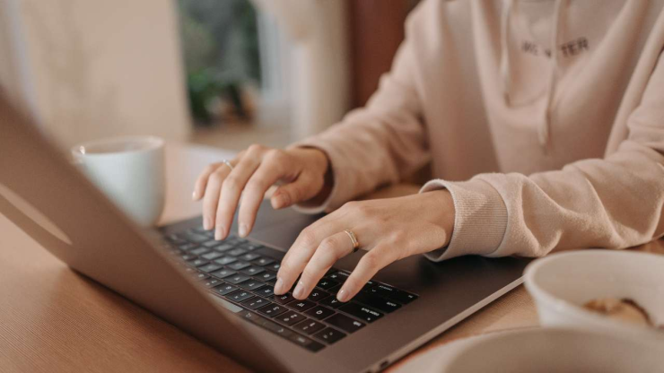 Sieviete strādā pie datora mājās un izstrādā jauno CV un motivācijas vēstuli, jo ir darba meklējumos