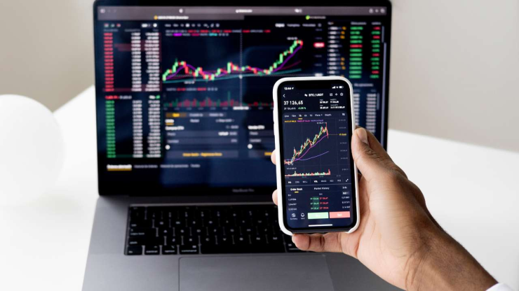Dators un telefons ar ekrānos ieslēgtiem finanšu tirgus grafikiem un cenu svārstībām