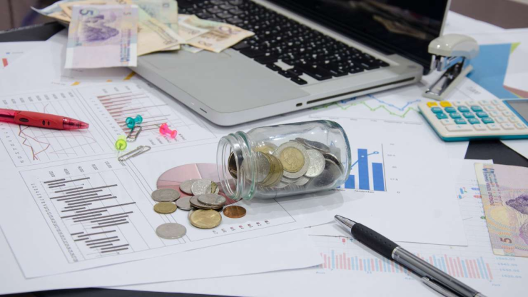 Attēlā naudas kaudzīte, kalkulators un grafiki, kas parāda finanšu analīzes un naudas ieguldīšanas un plānošanas procesu