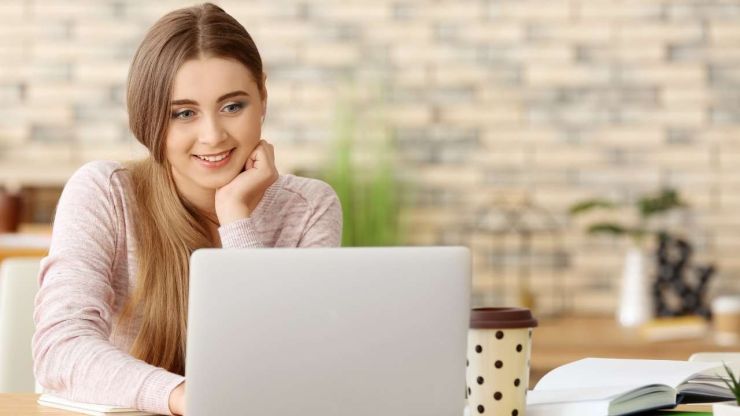 Девушка сидит за учебниками и ищет в ноутбуке, где можно взять кредит с 18 лет