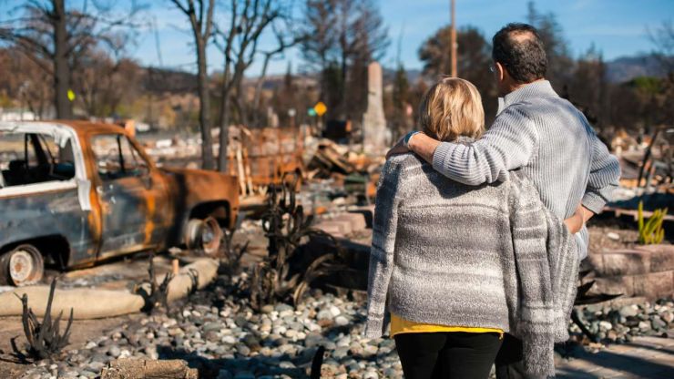 Муж с женой смотрят на разрушенный после стихийного бедствия дом, но рады, что имущество было застраховано