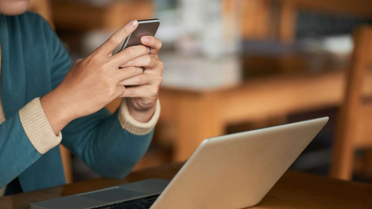 Человек использует смартфон перед ноутбуком, возможно, для оформления кредита без официального трудоустройства
