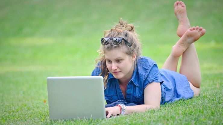 Девушка лежит на травке в парке и через ноутбук ищет все кредиты онлайн, чтобы их удобно сравнить в одном месте