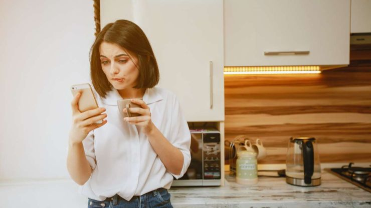 Девушка на кухне пьют кофе и параллельно ищет в телефоне, где оформить кредит с 20 лет