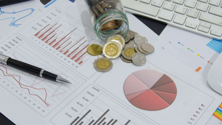 На столе графики инвестиций, банка с монетами и ручка – Скорпионы обдумывают куда вложить деньги в ноябре 2023 года