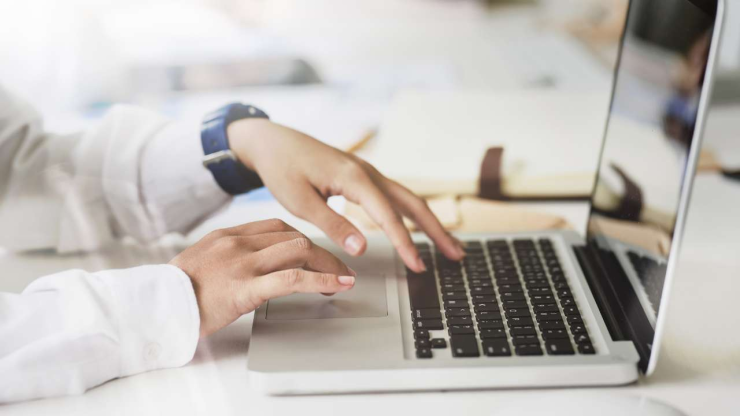 Руки человека набирают текст на ноутбуке, что связано с поиском информации о кредите без официального трудоустройства