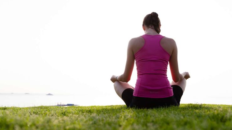 Sieviete sēž dabā pļavā un meditē, jo cenšas mazināt dzīves radīto finansiālo stresu