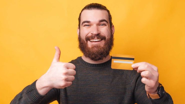 Vīrietis plati smaida un ar vienu roku rāda žestu ar īkšķi paceltu uz augšu, bet otrā tur kredītkarti ar piešķirto kredītlīniju