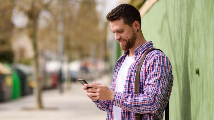 Мужчина стоит на улице и в телефоне ищет информацию, где получить быстрый кредит без проверки кредитной истории