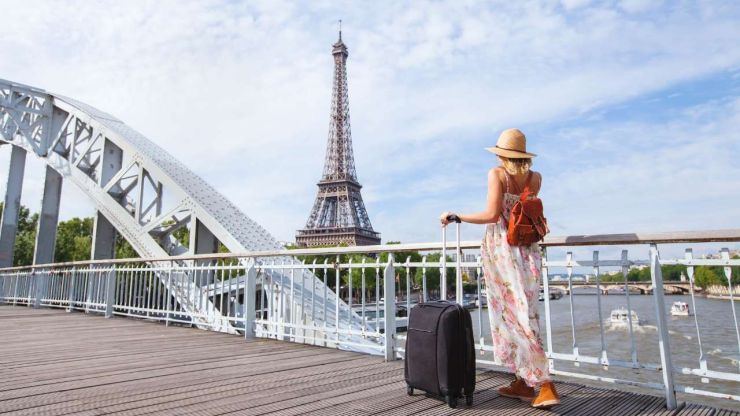 Sieviete ar koferi stāv uz tilta un skatās uz Eifeļa torni, jo, organizējot savas finanses, aizlidoja ceļojumā uz Parīzi