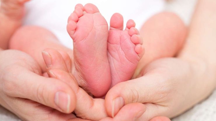 Māte, kas saņem paredzētos pabalstus, savās rokās tur sava jaundzimušā bērna kājiņas