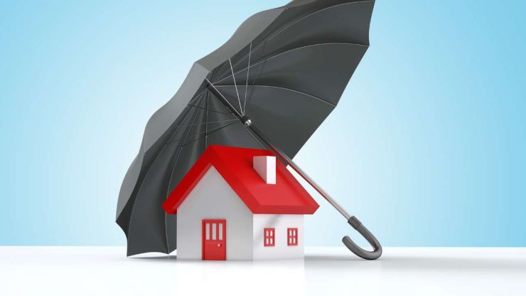 Белый домик с красной крышей, который прикрывает черный зонтик , поскольку страхование уберегает от финансового стресса