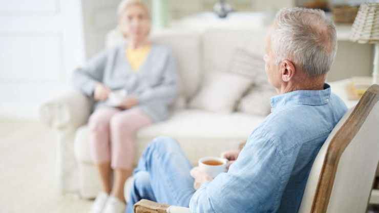Пожилые мужчина и женщина сидят на диванах, пью чай и рассуждают, какого управляющего выбрали для второго пенсионного уровня