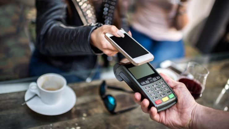Sieviete sēž kafejnīcā un norēķinās par savu izdzerto kafiju ar bezskaidras naudas norēķina veidu – mobilo maksājumu