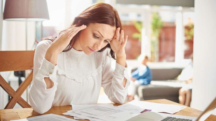 Sieviete, sēžot pie galda, pārskata savus rēķinus, lai samazinātu izdevumus, jo vēlas pārvarēt finanšu grūtības