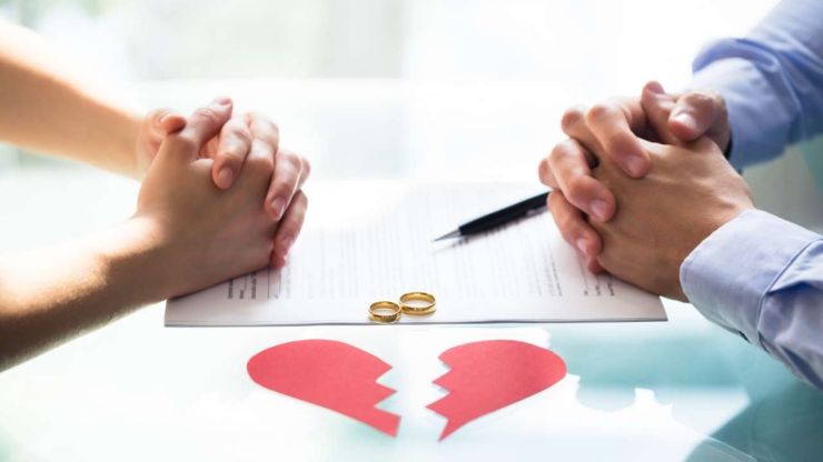 Vīrietis un sieviete pie pārrunu galda, nolikuši savus laulības gredzenus, lai vienotos par laulības šķiršanas izmaksām