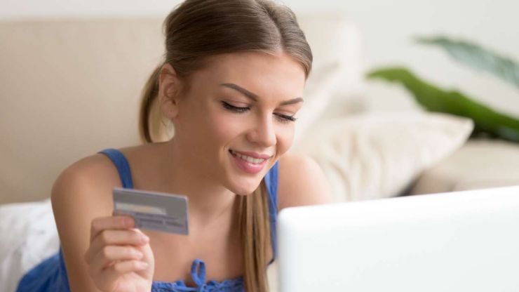 Девушка держит в руке банковскую карту и улыбается, так как у нее получилось оплатить покупку цифровым платежом, отказавшись от наличных денег