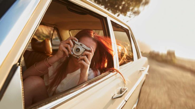 Девушка сидит в машине и через открытое окно делает снимок достопримечательности, так как отправилась заграницу, оформив кредит на путешествие