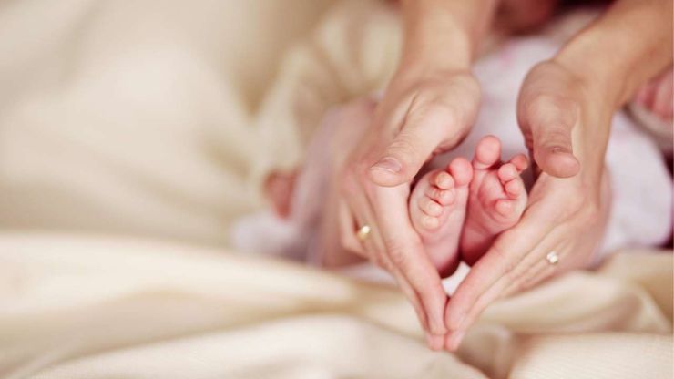 Мама держит в руках ножки своего новорожденного ребенка – теперь она может подать заявку на вторую часть декретных денег