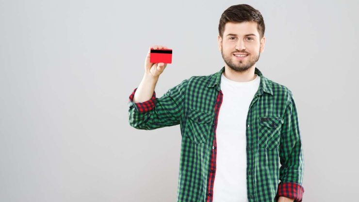 Smaidīgs vīrietis rūtainā kreklā tur rokās sarkanu kredītkarti, kurā ir ieskaitīts īstermiņa kredīts