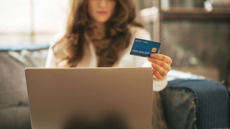 Sieviete aplūko savu kredītkarti, jo tikko izlasīja informāciju par debetu un kredītu, kā arī uzzināja atšķirību starp banku kartēm
