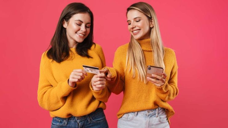 Jauniete ar telefonu rokā stāsta otrai jaunietei ar kredītkarti par iespējām, ko sniedz ilgtermiņa aizdevums