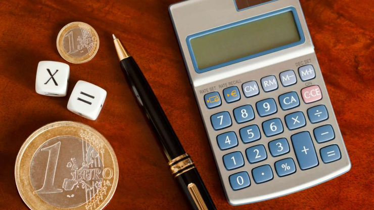 На деревяном столе натюрморт их евро монет, кубиков, ручки и калькулятора – необходимое для расчитывания 1 пенсионного уровня