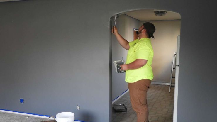 Мужчина красит стены в квартире, поскольку ремонт является хорошим вкладом денег в октябре 2023 года