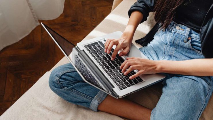 Sieviete sēž uz gultas un meklē datorā, kur paņemt ārkārtas situācijai piemēroto kredītu 