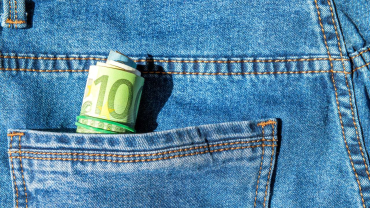 Купюра в десять евро, выглядывающая из кармана джинсов, иллюстрирующая повседневные расходы со средней зарплаты в Латвии