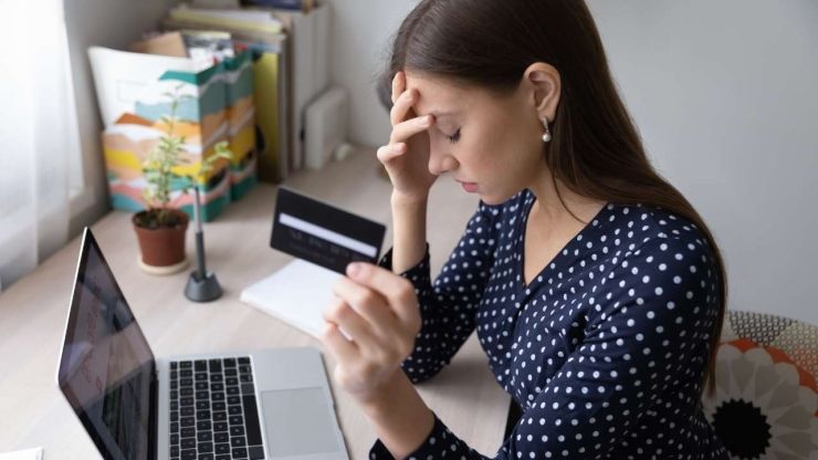 Sieviete sēž pie datora un meklē, kā uzlabot kredītvēsturi, jo kredītkarte, ko viņa tur rokās, ir tukša