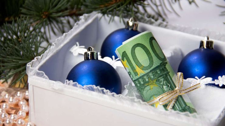 Белая подарочная коробка под елкой с синими елочными игрушками и купюрой в сто евро, перевязанной ленточкой – лучший вариант оформить денежный подарок