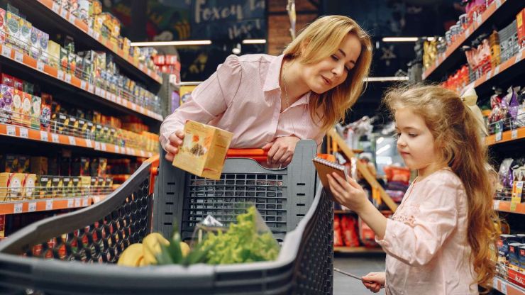 Māte ar meitu veikalā veic pirkumus, pieturoties sarakstam un izvēloties lētākas alternatīvas