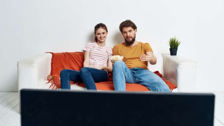 Парень с девушкой сидят на диване и смотрят хоккей на новом телевизоре, который купили благодаря всем кредитам онлайн