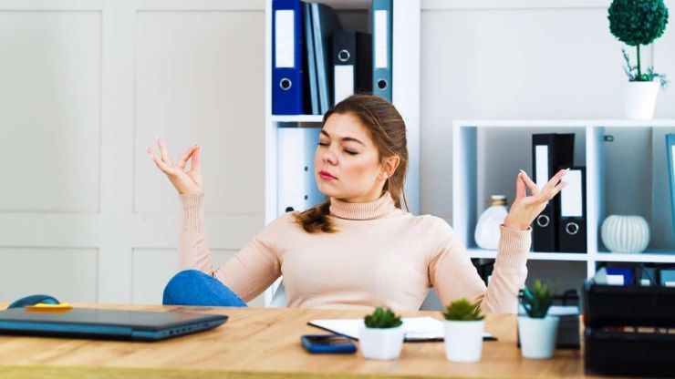 Девушка за офисным столом медитирует, потому что не поддается панике при финансовых проблемах