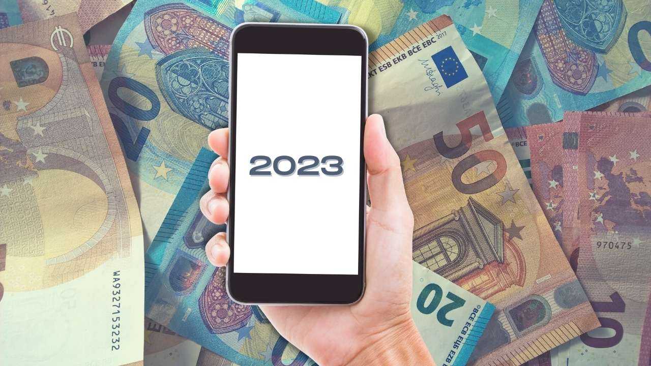 Fonā eiro banknotes minimālās algas apmērā un priekšā roka ar telefonu, uz kura ekrāna ir uzraksts “2023”