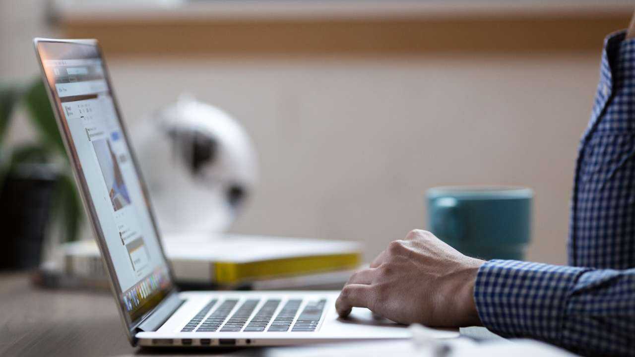 Мужчина сидит за столом и ищет через ноутбук в интернете информацию, как стать самозанятым лицом