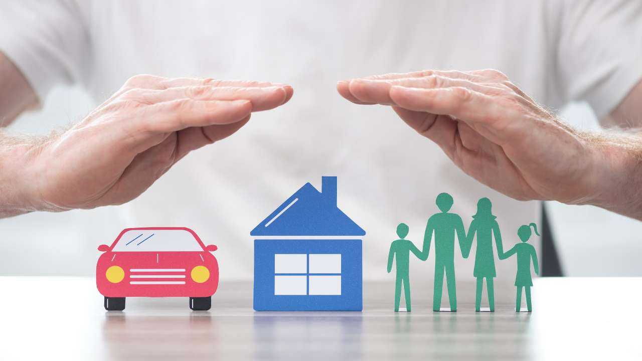 На столе стилизованная машина, дом и семья, которые накрывают руки как крышей – важно оформить страховой полис
