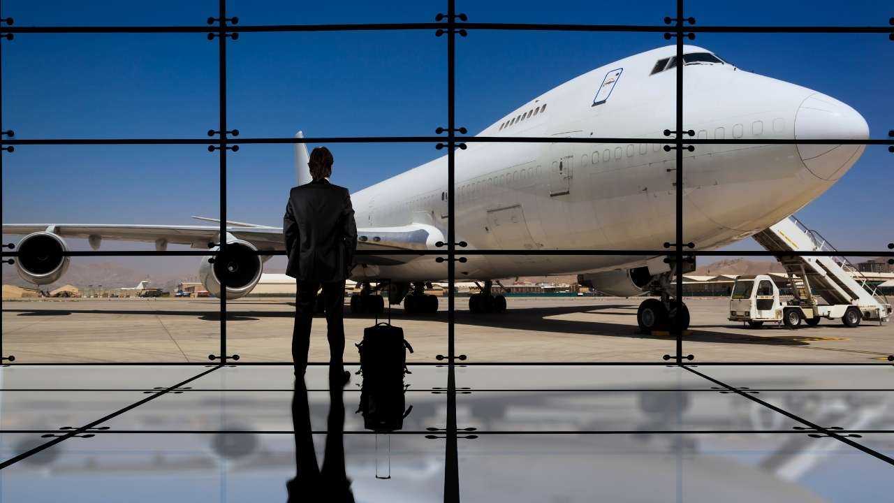 Vīrietis ar čemodānu gaida savu lidmašīnu, jo brauc darba braucienā, par ko viņam maksās komandējuma naudu