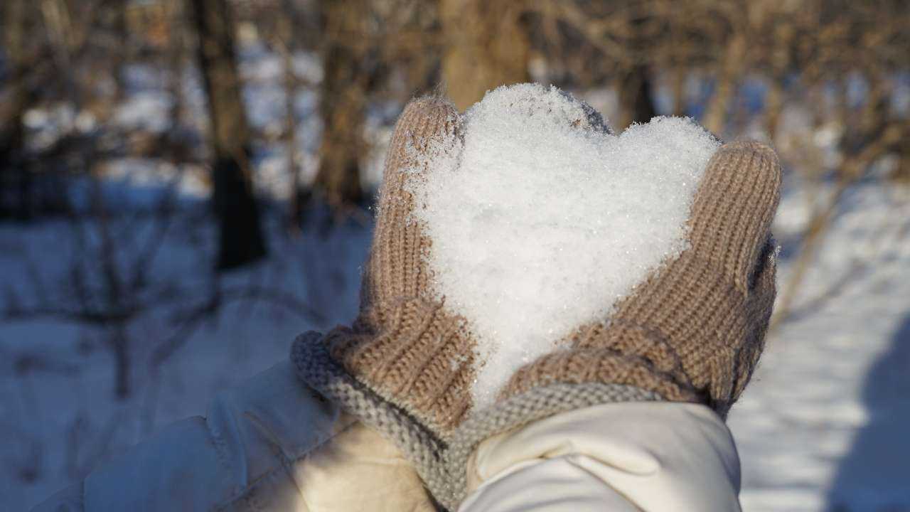 Rokas ziemas dūraiņos ar sirds formā saliktu sniegu, kas simbolizē naudas horoskopu 2024. gada februārim