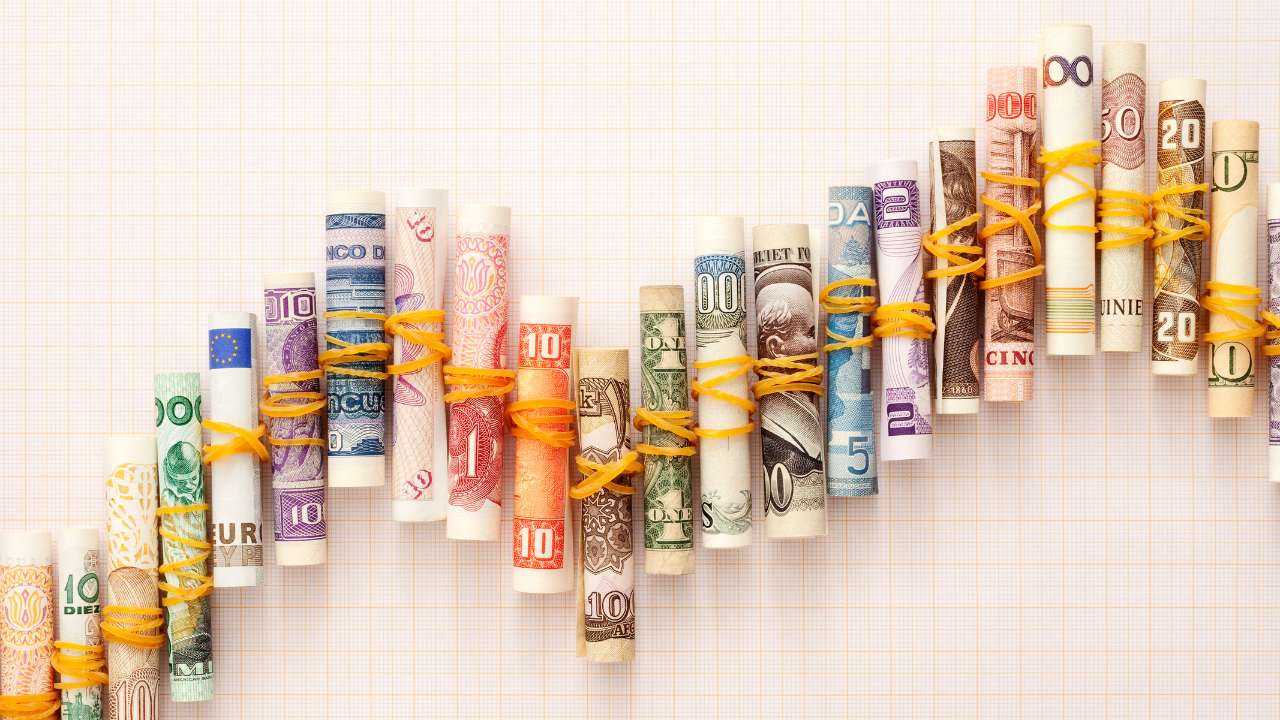 Dažādu valstu naudas banknotes, satītas tūtiņā un pārsietas ar gumiju, saliktas neregulārā līnijā, tādejādi parādot valūtas kursu svārstības