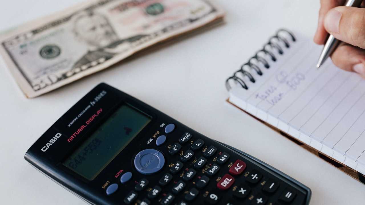 Persona veic savas bruto algas aprēķinus, izmantojot kalkulatoru un piezīmju blociņu