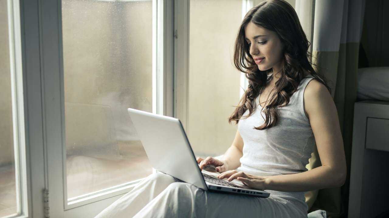 Sieviete sēž uz palodzes un datorā meklē, kurš kreditors piedāvā viņai nepieciešamo patēriņa kredīta summu