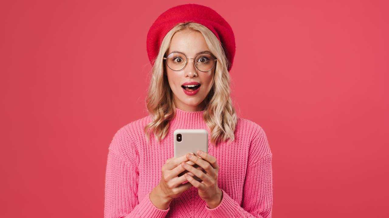 Девушка в розовой шляпке радостно удивлена, что нашла через телефон в интернете выгодный первый кредит бесплатно