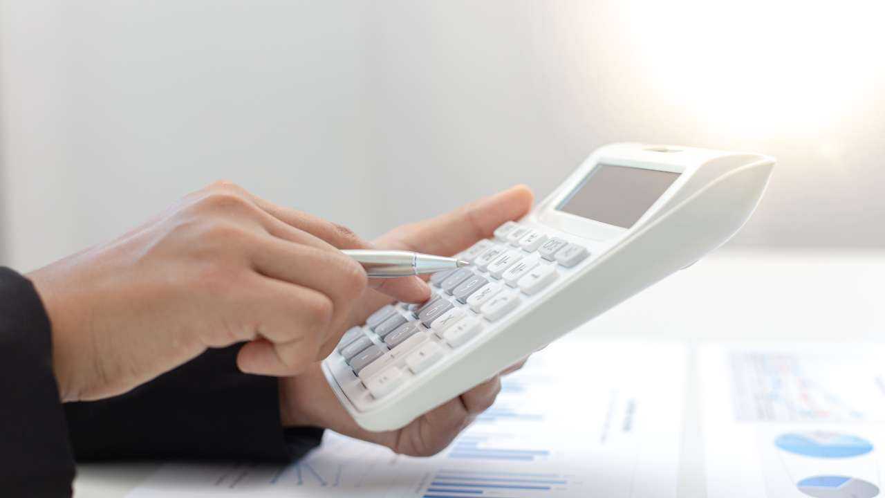 Persona, turot rokā pildspalvu, uz kalkulatora rēķina savu parādsaistību summu, lai tos veiksmīgi pārvaldītu