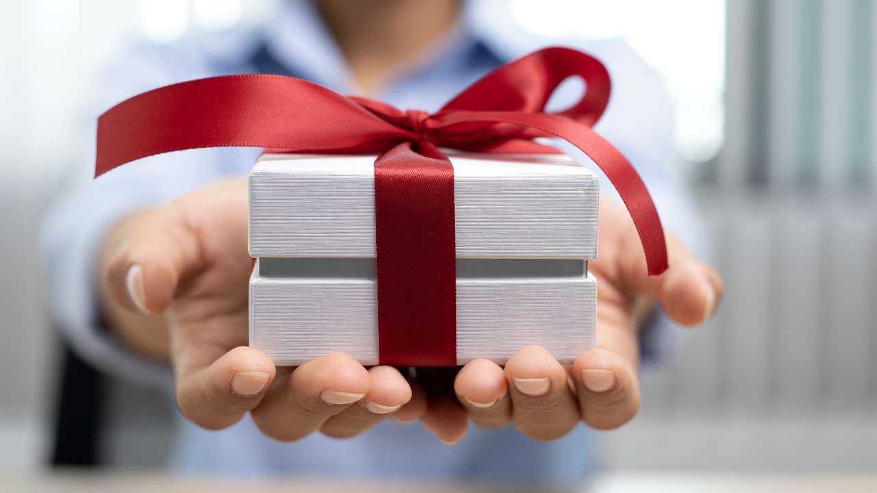 Девушка оформила денежный подарок и теперь его преподносит в красивой белой коробке с красным бантом