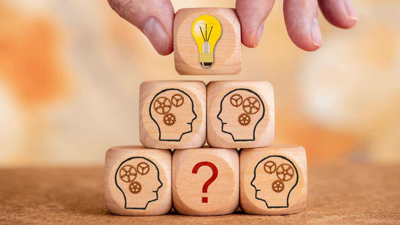 Кубики с изображениями голов с шестеренками и лампочкой с немым вопросом: «Финансовое решение: принимаем или откладываем?»